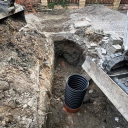 hidroallpl - Wykop pod instalację z widoczną karbowaną rurą kanalizacyjną, obok sterta kostki brukowej i fragment koparki.