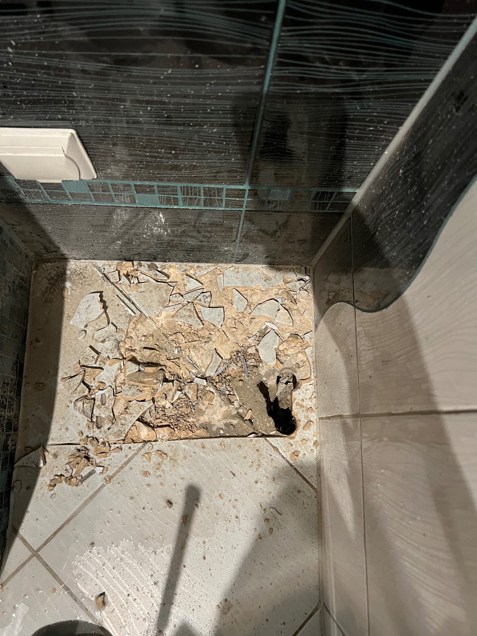 Zniszczona podłoga w kabinie prysznicowej w Piasecznie, z widocznym otworem w posadzce i resztkami potłuczonych płytek.