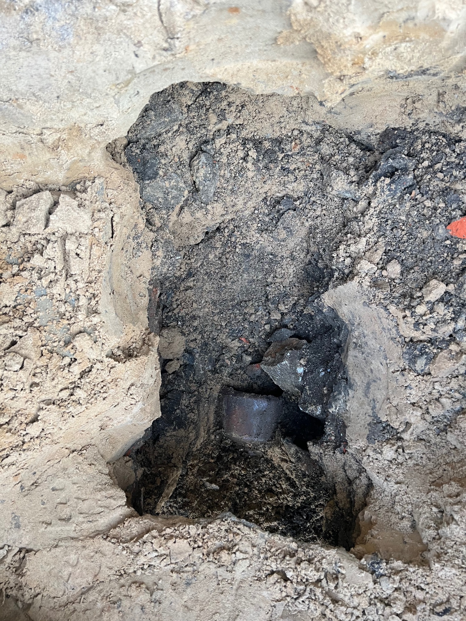 Wykop w ziemi z widoczną rurą kanalizacyjną, otoczony gruzem i ziemią.