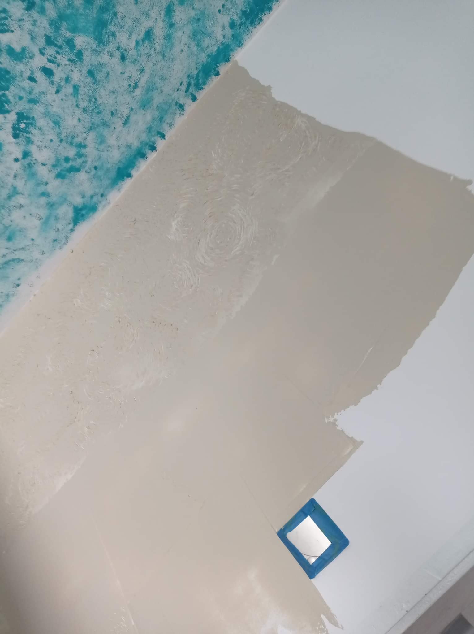 Fragment sufitu w trakcie prac wykończeniowych, z widocznymi śladami szpachlowania i malowania, częściowo pokryty turkusową farbą dekoracyjną, zabezpieczony otwór taśmą malarską.