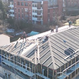 STONEROOF RAFAŁ ZIÓŁKOWSKI - Ekipa montuje łatowanie dachu na budynku w zabudowie miejskiej. Widoczne rusztowania i przygotowane deski. Praca w toku, z perspektywy z góry.