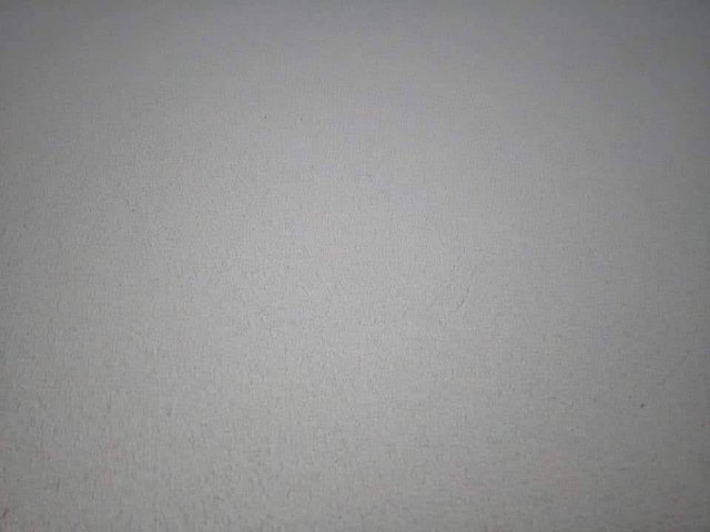 Szara, gładka powierzchnia ściany z delikatną fakturą, oświetlona z góry, widoczne drobne niedoskonałości i zacieki.