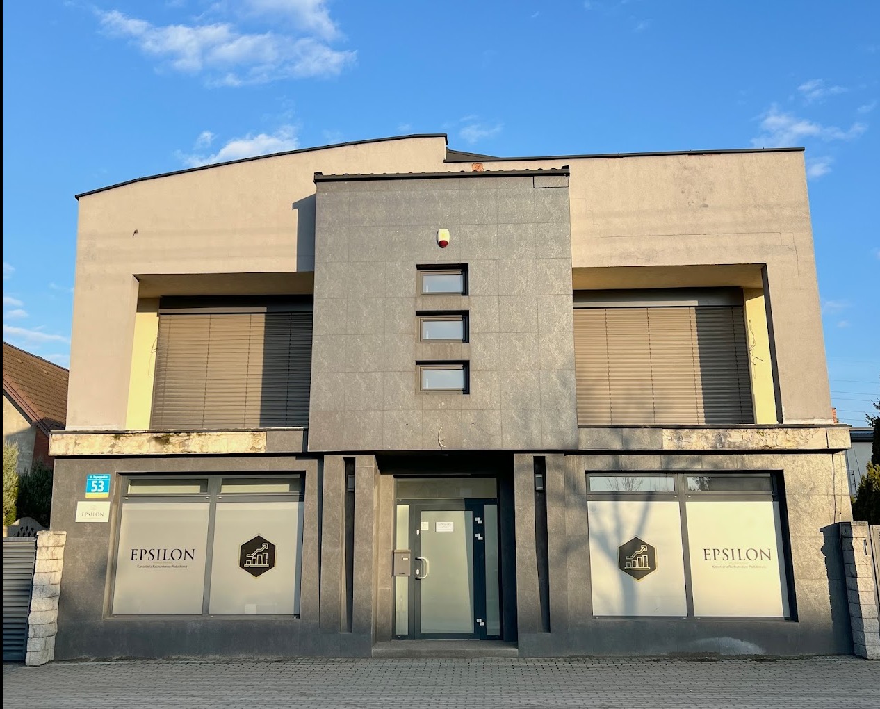 Dwupiętrowy budynek biurowy z logo 'Epsilon' na oknach, sugerujący siedzibę firmy księgowej lub doradczej, z numerem budynku 53.