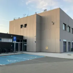 Wejście do filii kancelarii prawnej w budynku dworca, z widocznymi miejscami parkingowymi dla osób niepełnosprawnych oznaczonymi niebieskimi symbolami na asfalcie, stojakami na rowery i szyldem...