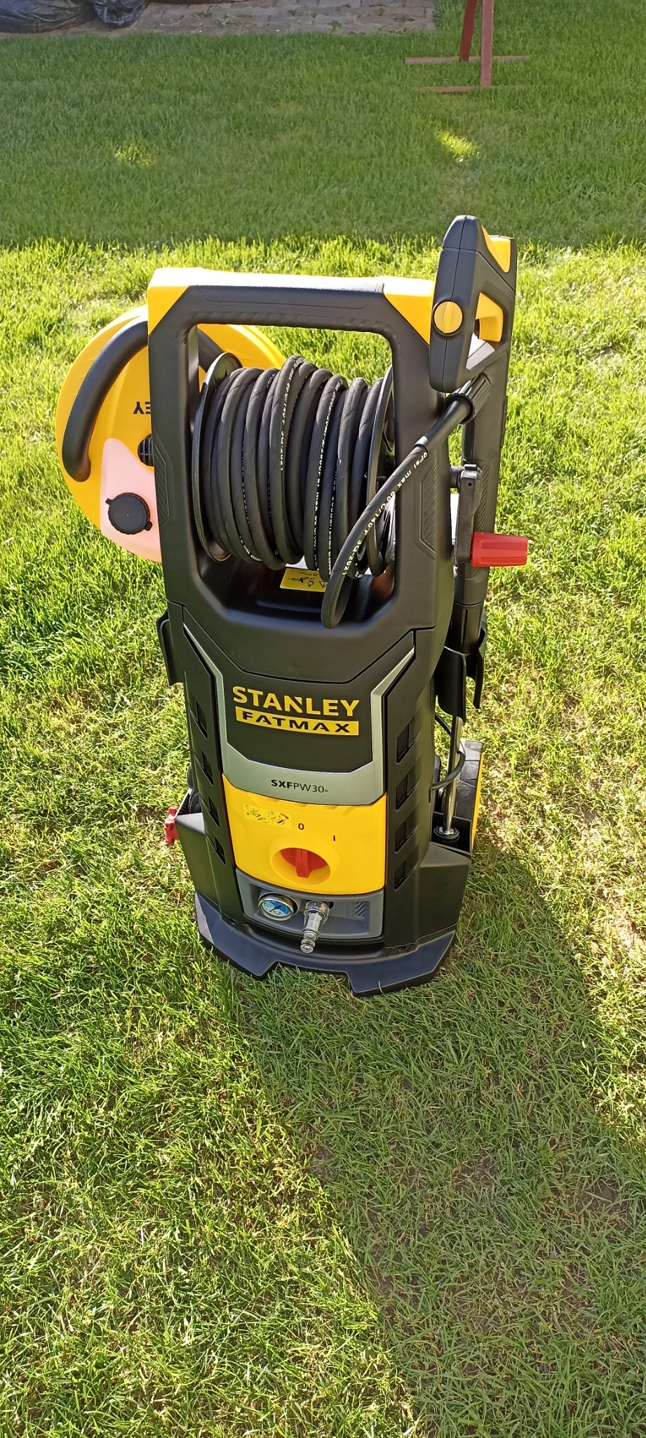Żółto-czarna myjka ciśnieniowa Stanley Fatmax SXFPW30 na trawie, z nawiniętym wężem i widocznymi elementami sterującymi.
