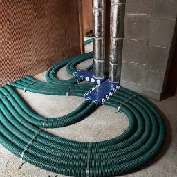 Wentplast - Rozprowadzona instalacja rekuperacji z zielonymi rurami i niebieskimi rozdzielaczami, widoczne dwa pionowe, zaizolowane przewody. Surowy stan budynku.