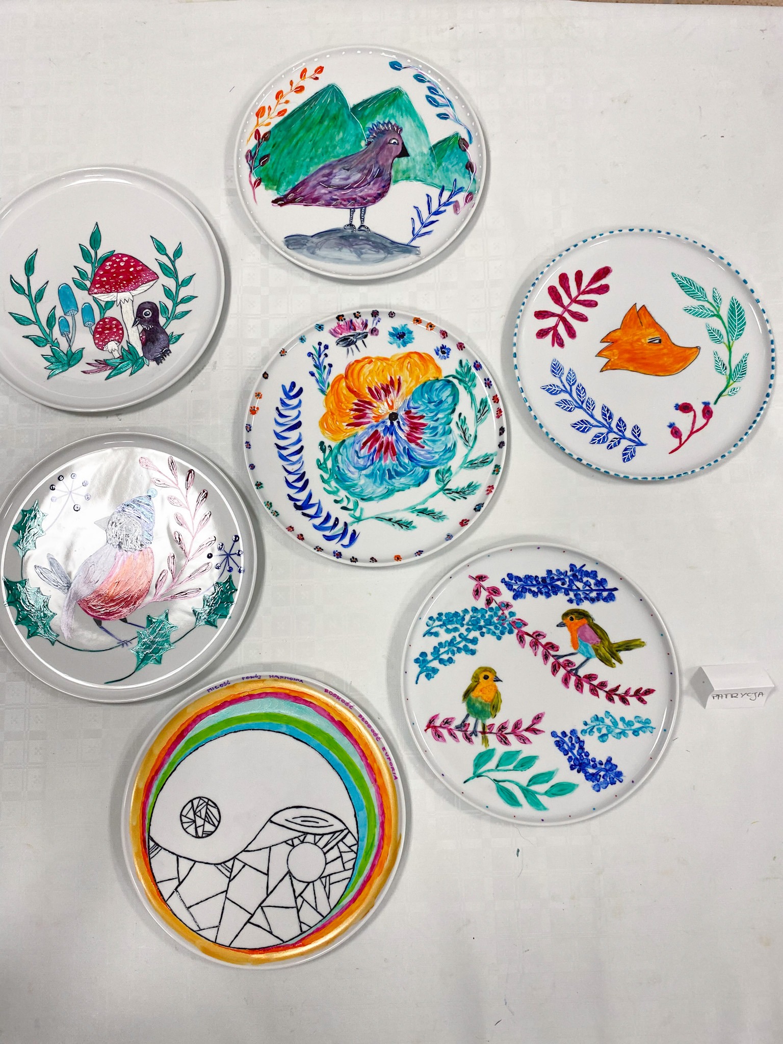 Ręcznie malowane, dekoracyjne talerze z motywami zwierzęcymi, roślinnymi i symbolami, ułożone na białym tle.