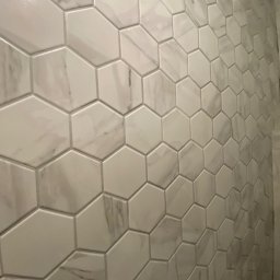 Yurii Yatsyshyn Yat-Fliz - Ściana wyłożona błyszczącymi, heksagonalnymi płytkami imitującymi marmur w łazience w Warszawie, widoczne subtelne żyłki i szare fugi.