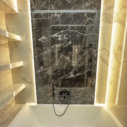 Yurii Yatsyshyn Yat-Fliz - Nowoczesna łazienka z wanną, czarnymi płytkami imitującymi marmur na ścianie z wnęką i podświetlanymi półkami z jasnego marmuru po bokach.