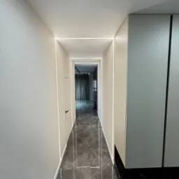 Korytarz z szarymi ścianami, podłogą z płytek imitujących marmur i oświetleniem LED wzdłuż krawędzi ścian i podłogi, perspektywa z głębi korytarza.