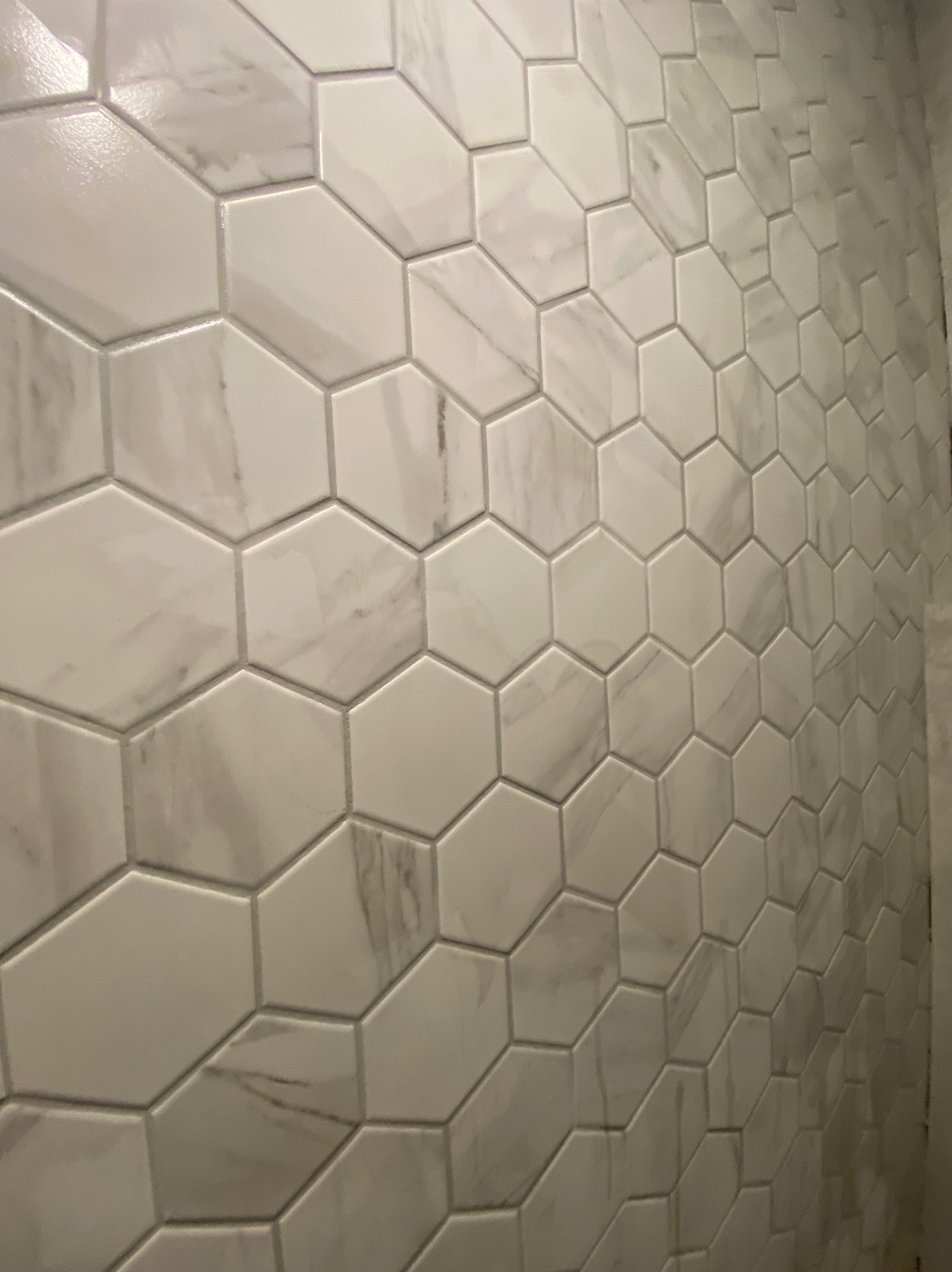 Ściana wyłożona błyszczącymi, heksagonalnymi płytkami imitującymi marmur w łazience w Warszawie, widoczne subtelne żyłki i szare fugi.