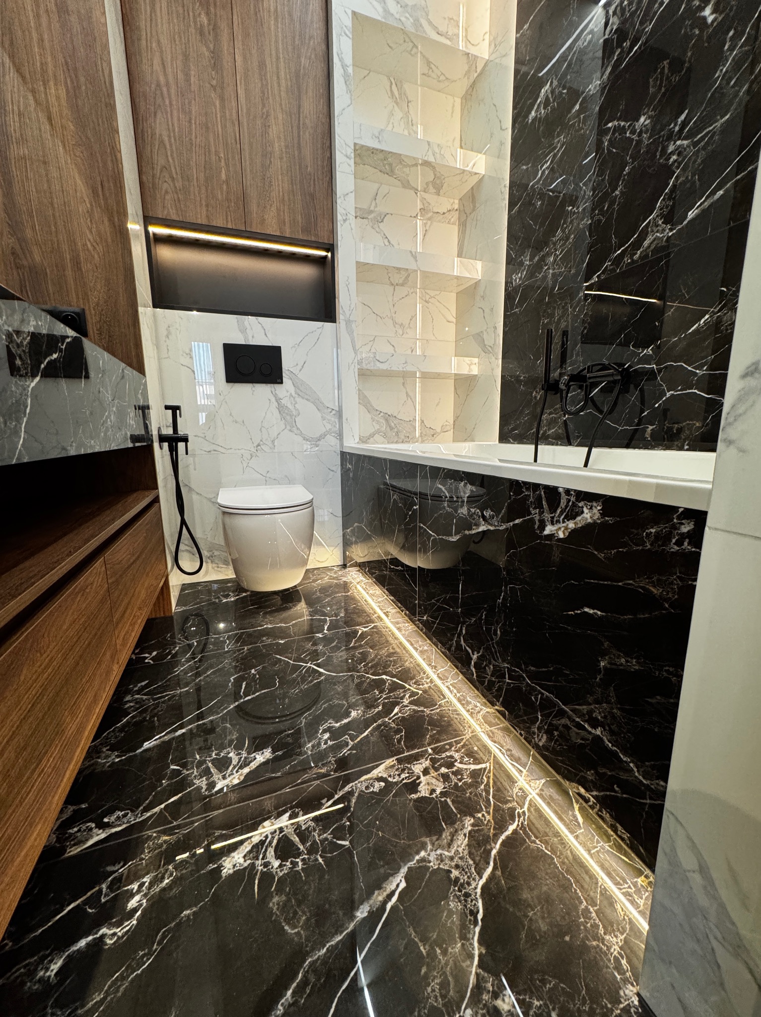Nowoczesna łazienka z czarną marmurową podłogą podświetloną listwą LED, drewnianą zabudową, białą ceramiką i czarną armaturą.