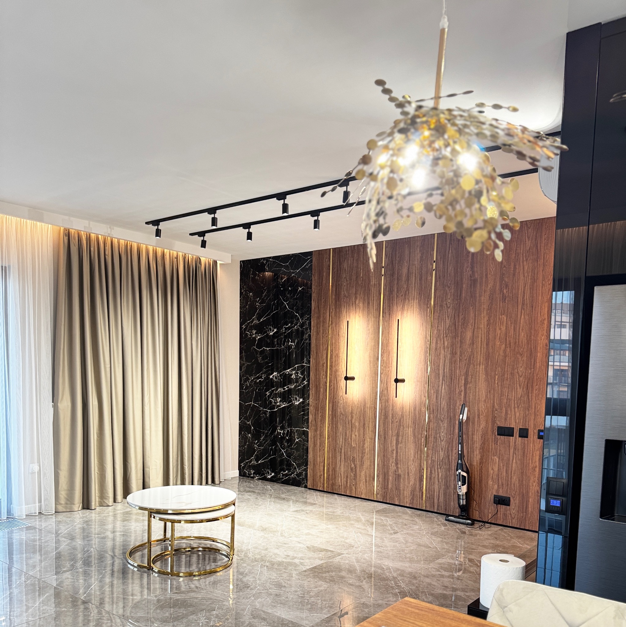 Eleganckie wnętrze salonu z marmurową podłogą, drewnianą okładziną ścienną z czarnym marmurowym akcentem, designerskim oświetleniem sufitowym i bocznym, oraz stolikiem kawowym z białym blatem...