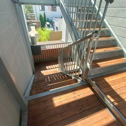 CleanWood - Zewnętrzne schody z drewnianymi stopniami i metalową konstrukcją prowadzące z tarasu na dół, widok z góry.