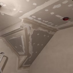 MARIAN PARZYGNAT MP-BUD FIRMA REMONTOWO-BUDOWLANA - Sufit poddasza po szpachlowaniu, widoczne łączenia płyt gipsowych i miejsca po wkrętach. Fragment drabiny malarskiej w lewym dolnym rogu kadru.