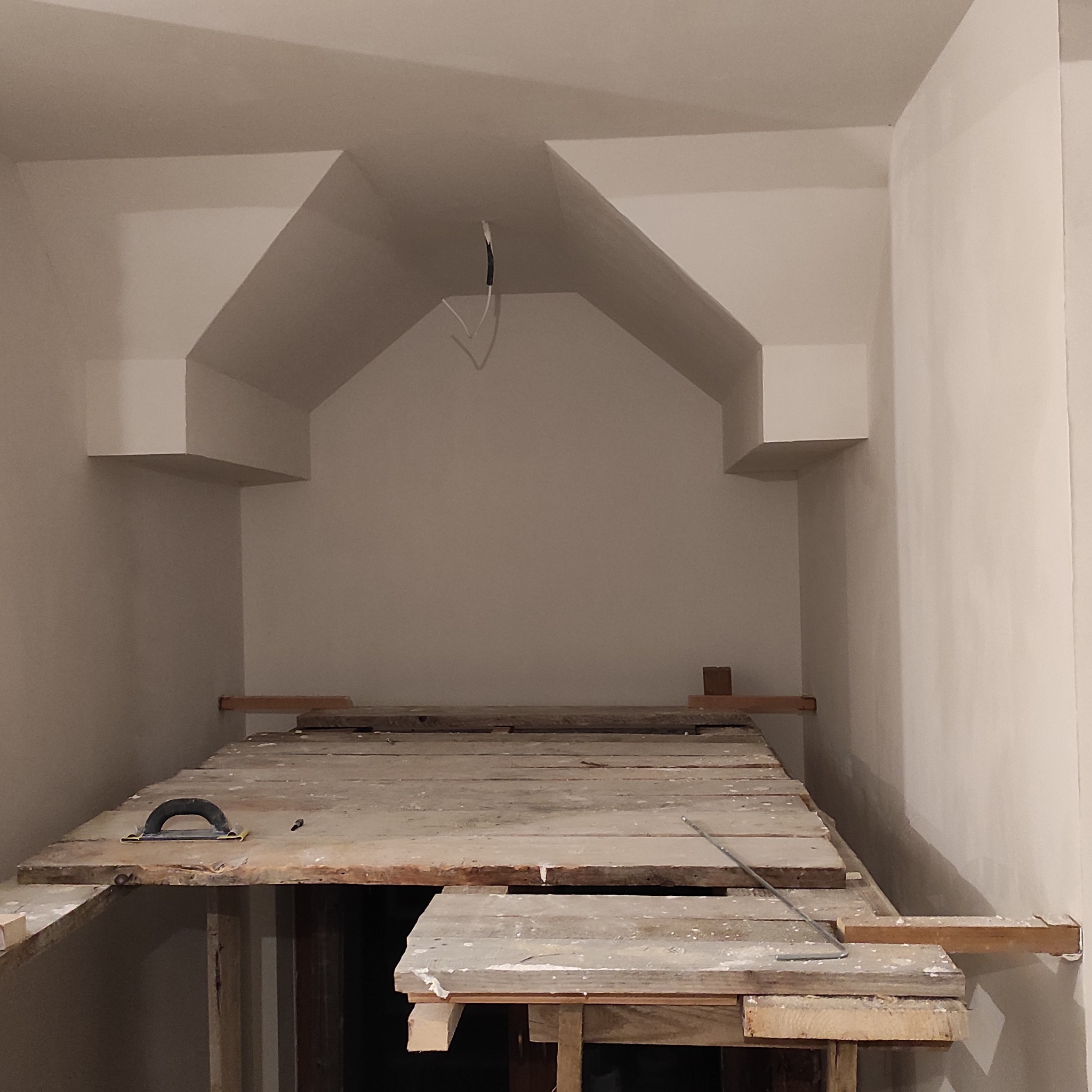 Wnęka z elementami dekoracyjnymi w trakcie wykańczania. Widoczne rusztowanie i narzędzia. Ściany w jasnym odcieniu, surowy stan.