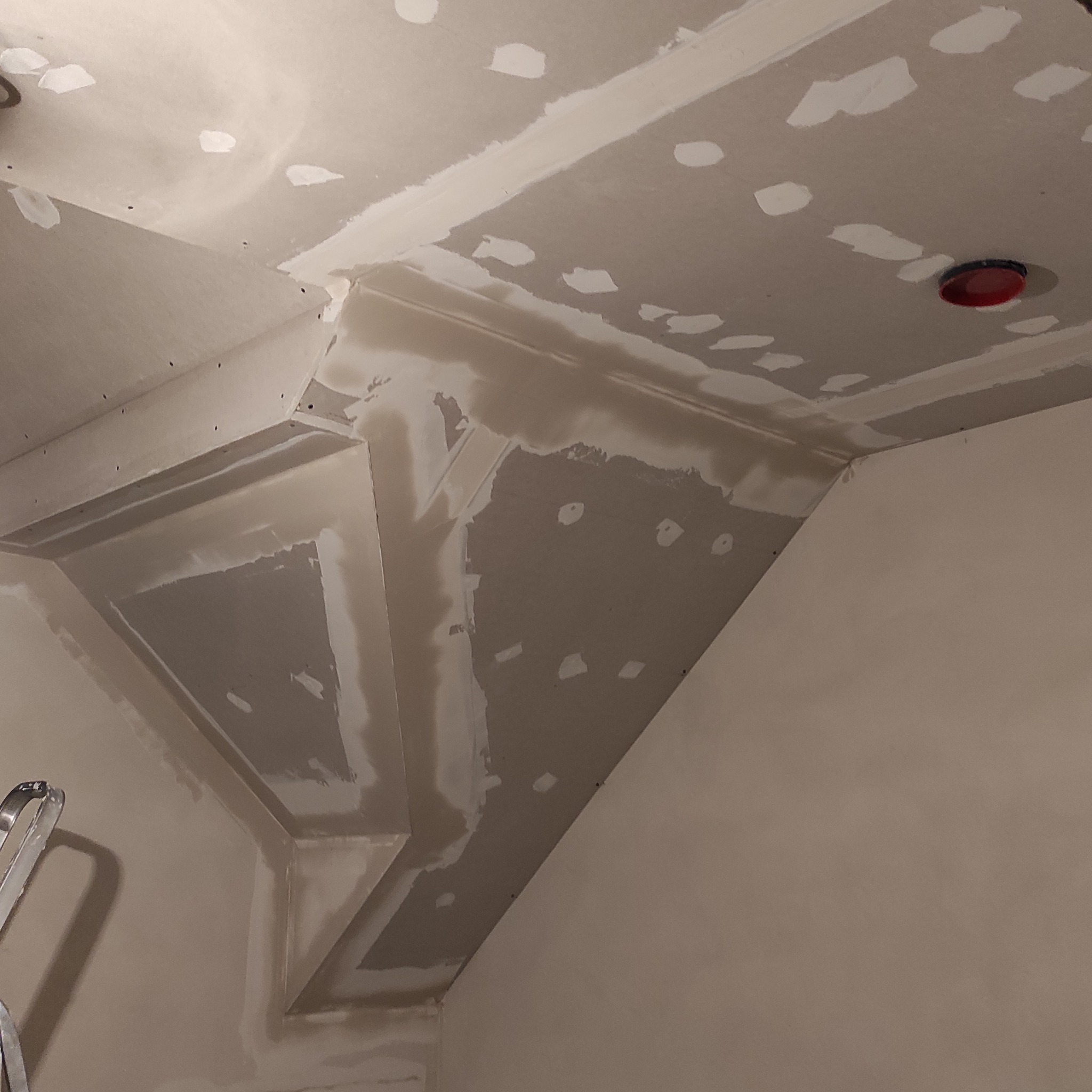 Sufit poddasza po szpachlowaniu, widoczne łączenia płyt gipsowych i miejsca po wkrętach. Fragment drabiny malarskiej w lewym dolnym rogu kadru.