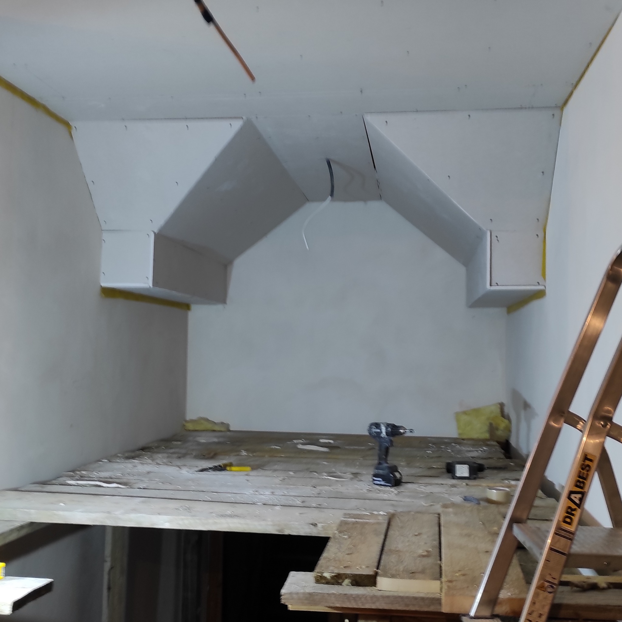 Sufit poddasza z konstrukcją z płyt gipsowo-kartonowych w trakcie montażu, widoczna drabina i narzędzia. Żółta taśma zabezpieczająca na krawędziach.