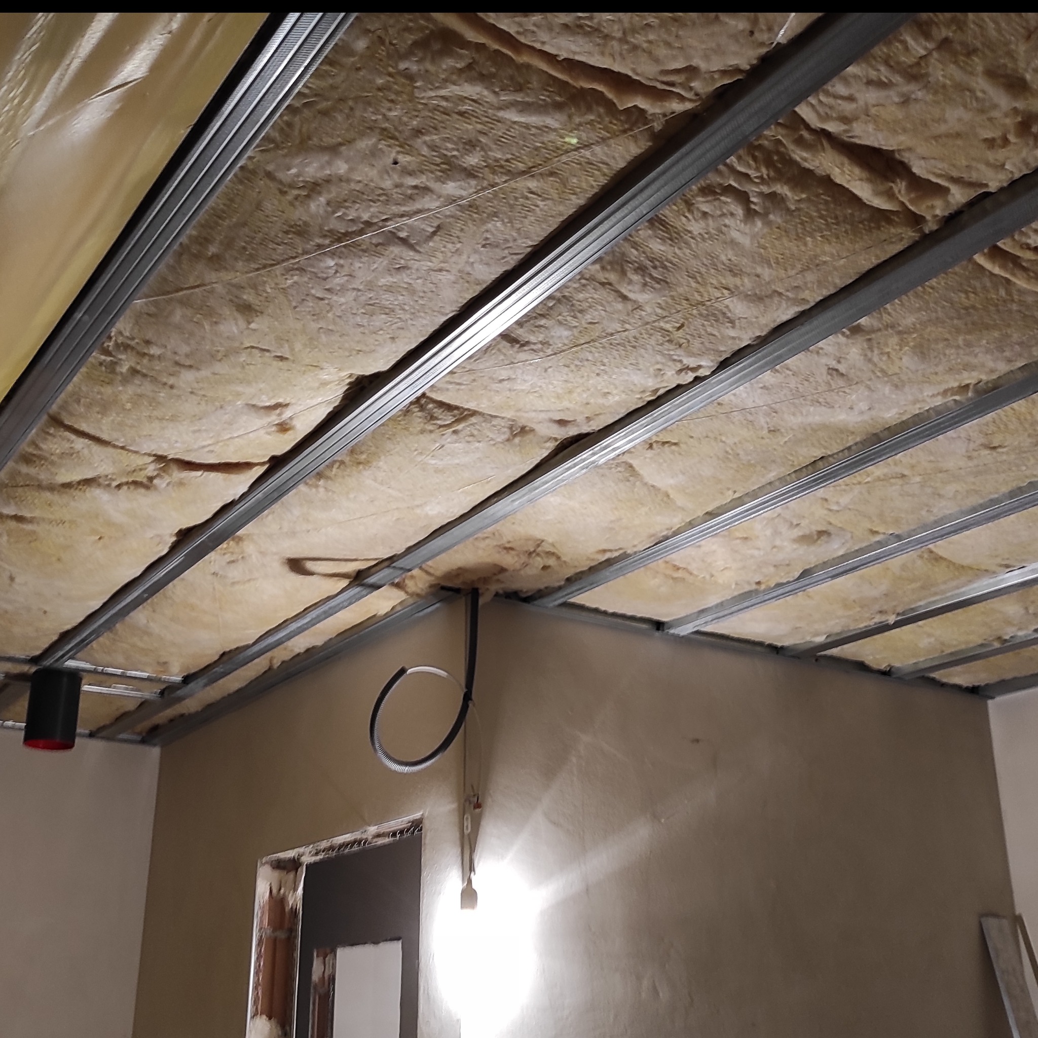 Ocieplenie poddasza wełną mineralną, widoczne metalowe profile konstrukcyjne. Fragment instalacji elektrycznej. Ściany w trakcie prac wykończeniowych.