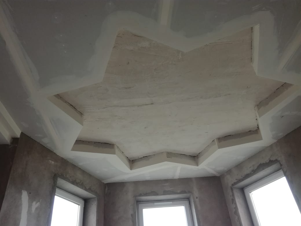 Sufit z płyt kartonowo-gipsowych uformowany w gwiazdę, widoczne łączenia i surowa powierzchnia przed wykończeniem, ściany w stanie deweloperskim z oknami.