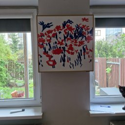 PROKLIM Łukasz Śliwiński - Biały grzejnik pod oknem z roletą, obok okno z widokiem na ogród. Na ścianie wisi obraz z motywem kwiatowym. Kot spogląda z parapetu.