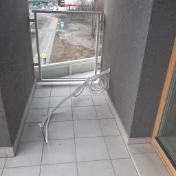 PROKLIM Łukasz Śliwiński - Białe kable klimatyzacji na balkonie z szarą, teksturowaną ścianą. Na zewnątrz widoczny pracownik w kamizelce. Kable częściowo zwisają.