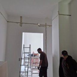 PROKLIM Łukasz Śliwiński - Instalacja elektryczna w surowym wnętrzu: widoczne przewody na ścianach, drabiny i dwóch mężczyzn w trakcie pracy. Realizacja w trakcie montażu.