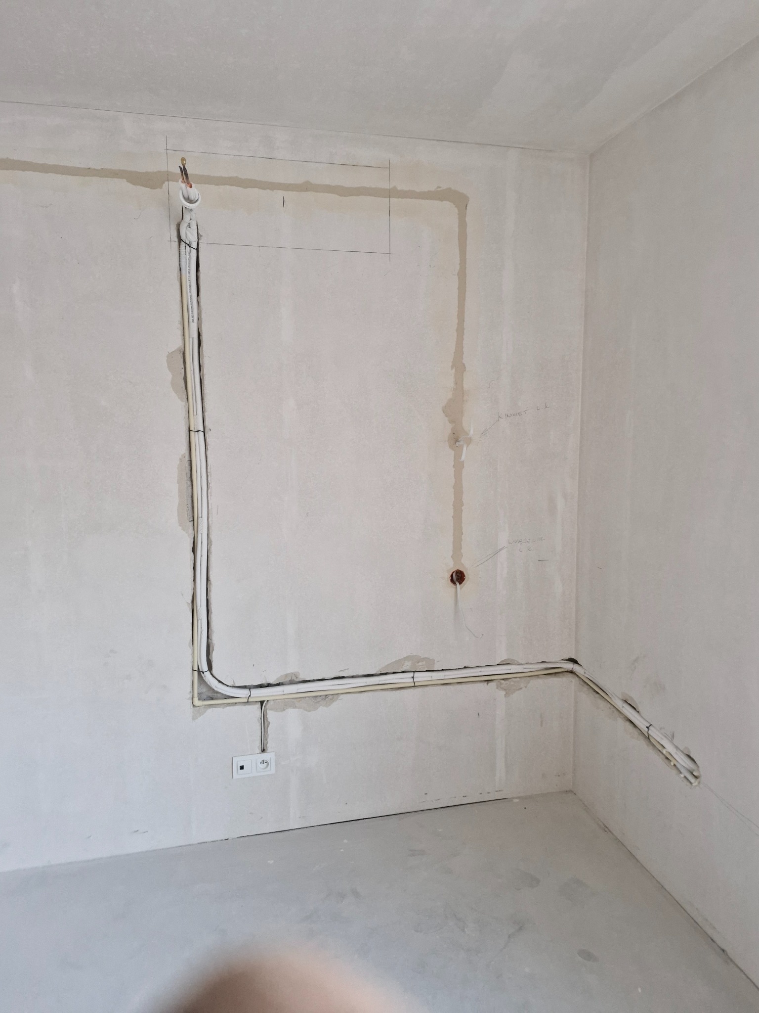 Instalacja przewodów wentylacyjnych i elektrycznych w surowym wnętrzu. Widoczne kable prowadzone po ścianach, gniazdko elektryczne i oznaczenia na ścianie.