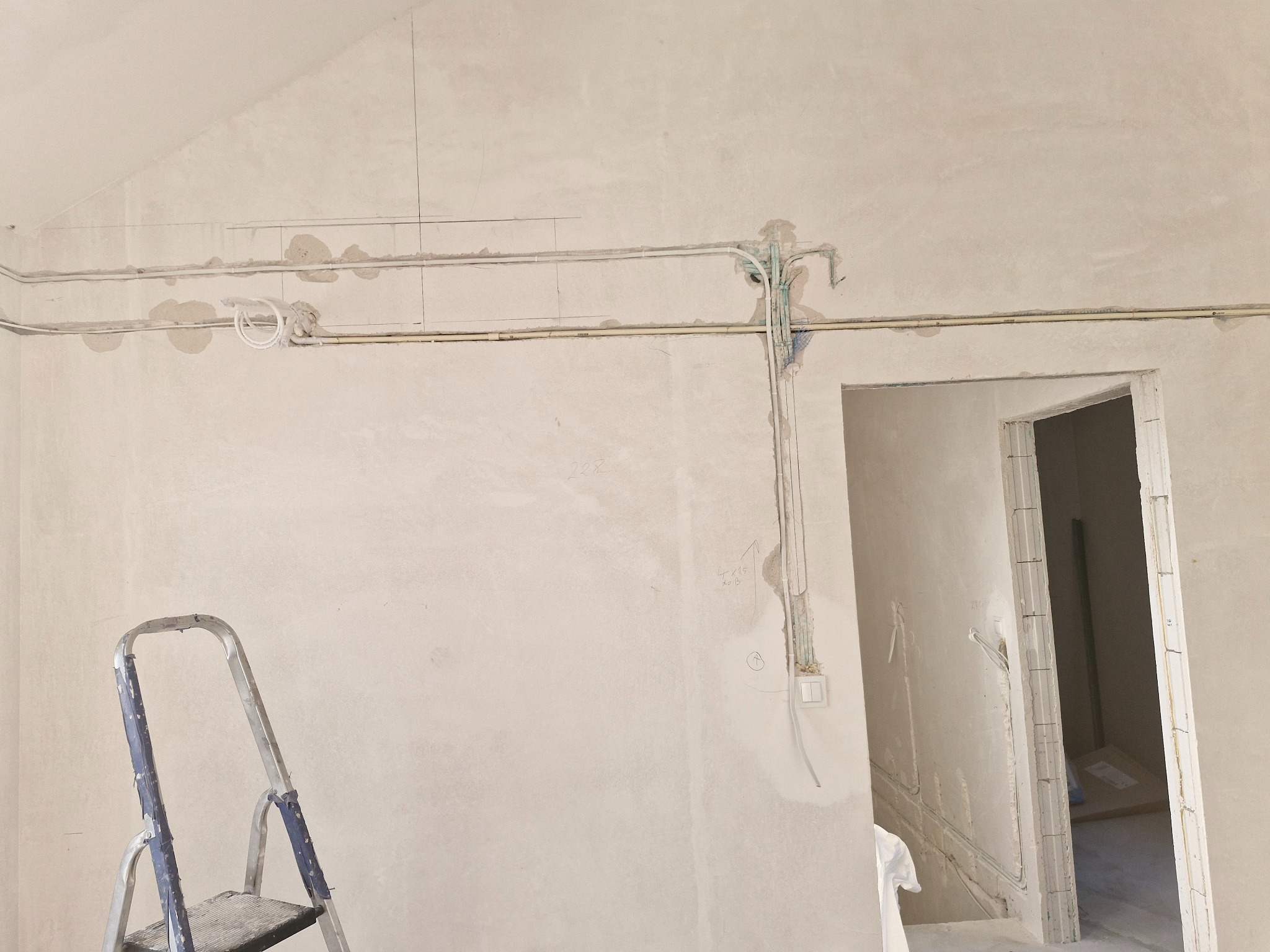Ściana w trakcie prac instalacyjnych: widoczne przewody elektryczne, puszki, drabina malarska. Surowy stan wykończenia wnętrza, przygotowanie do montażu klimatyzacji.