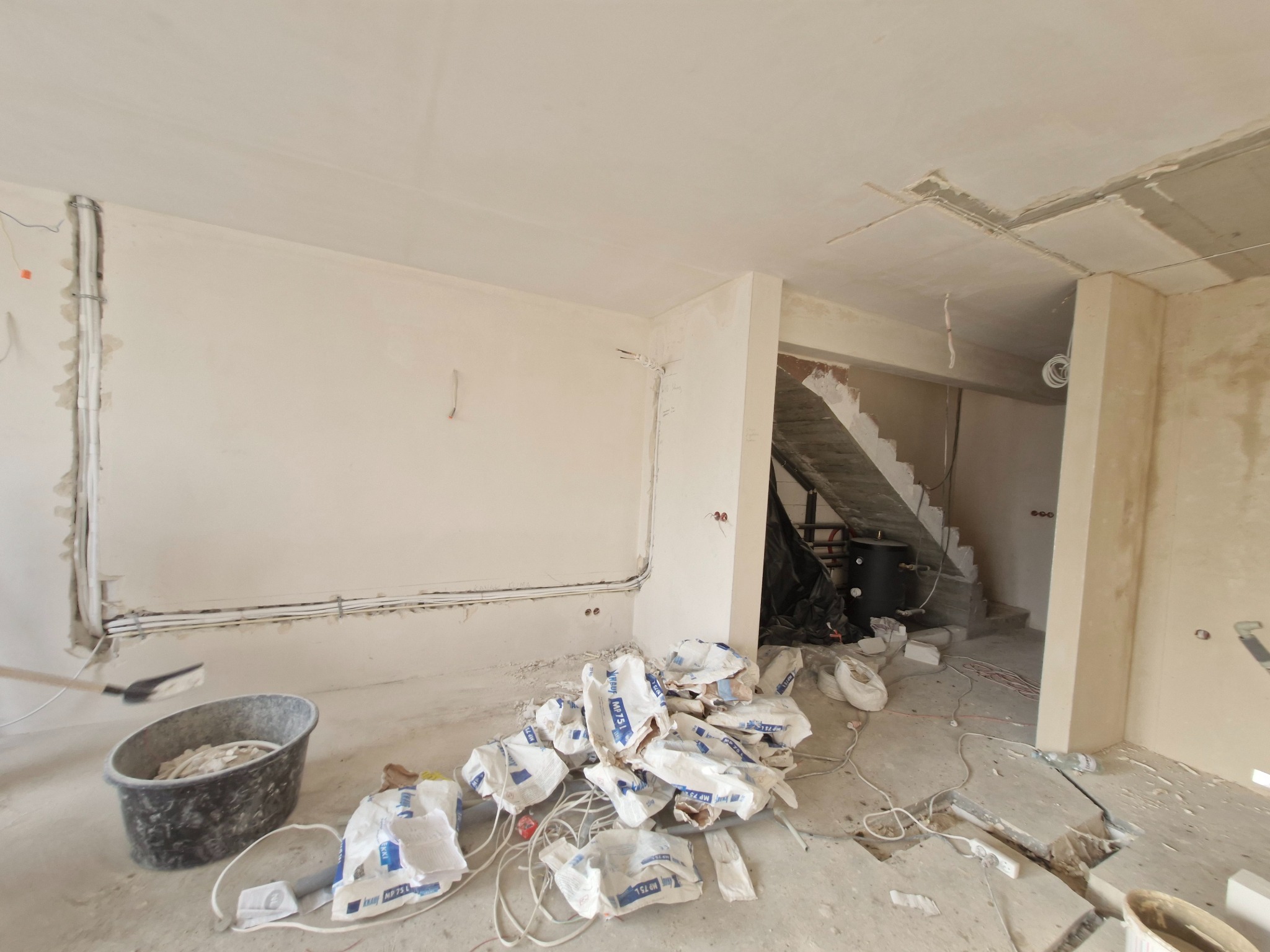 Stan surowy w Dąbrowie Chotomowskiej: ściany po instalacji, przygotowane do dalszych prac wykończeniowych, widoczne kable, worki z zaprawą i wiadro.