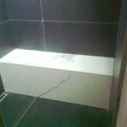 Wnętrze łazienki z ciemnymi płytkami ściennymi i podłogowymi, z siedziskiem wyłożonym białym marmurem z szarymi żyłami, widok z dołu.