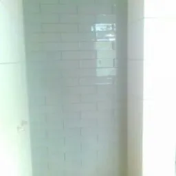 Ściana wyłożona jasnymi, prostokątnymi płytkami ceramicznymi z widocznymi fugami, odbijająca światło w łazience.