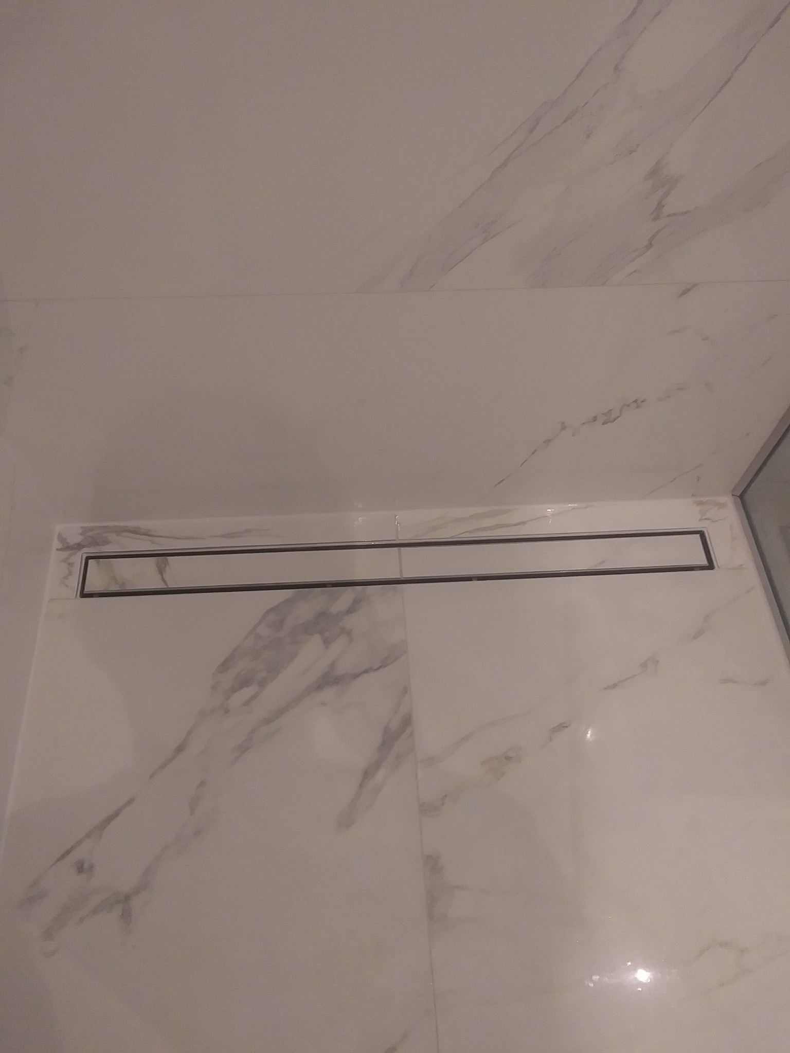 Białe płytki marmurowe z odpływem liniowym w kabinie prysznicowej, widok z góry pod kątem.