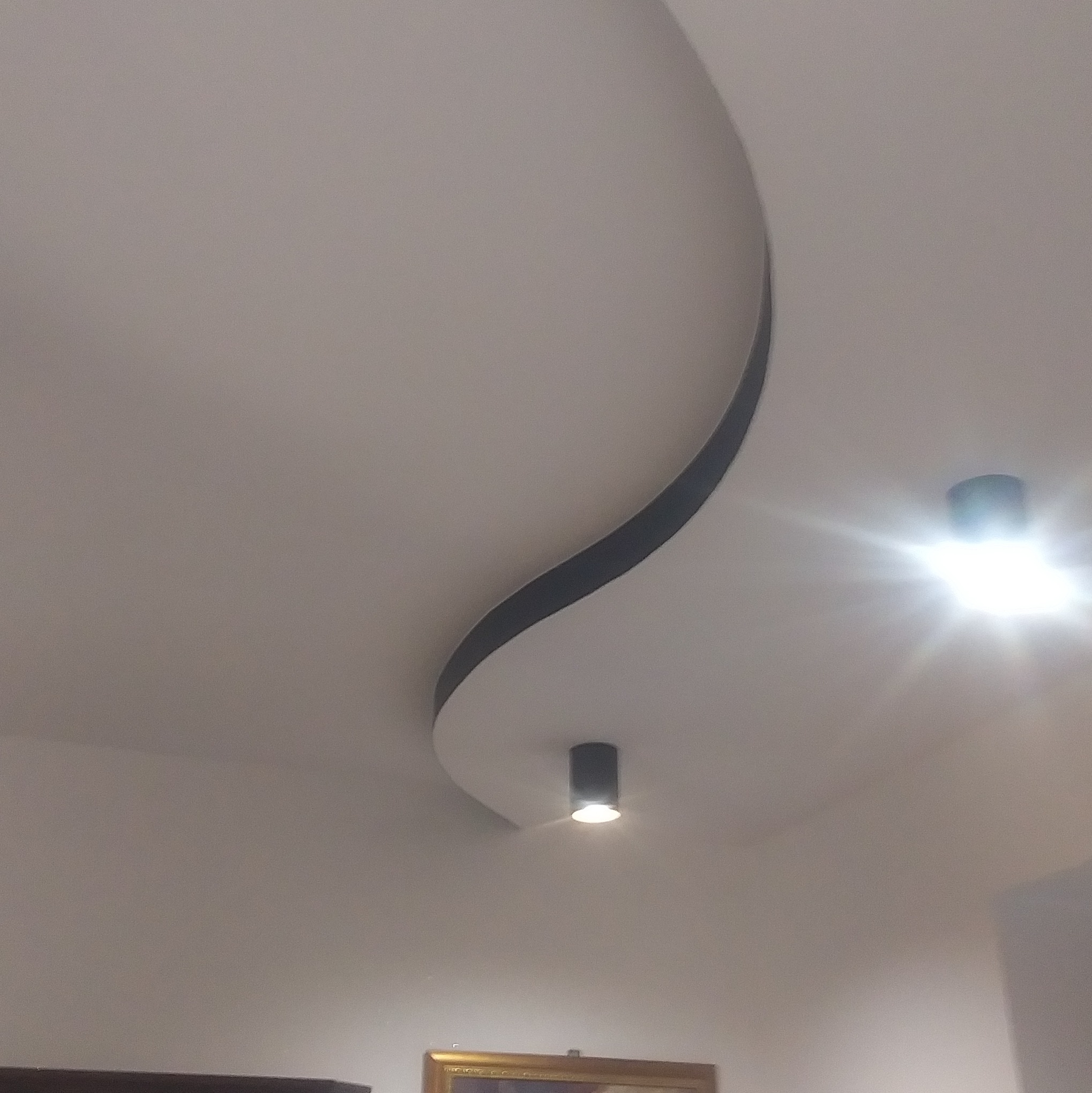 Nowoczesny sufit podwieszany z dekoracyjnym, zakrzywionym elementem i punktowym oświetleniem LED, widok z dołu.