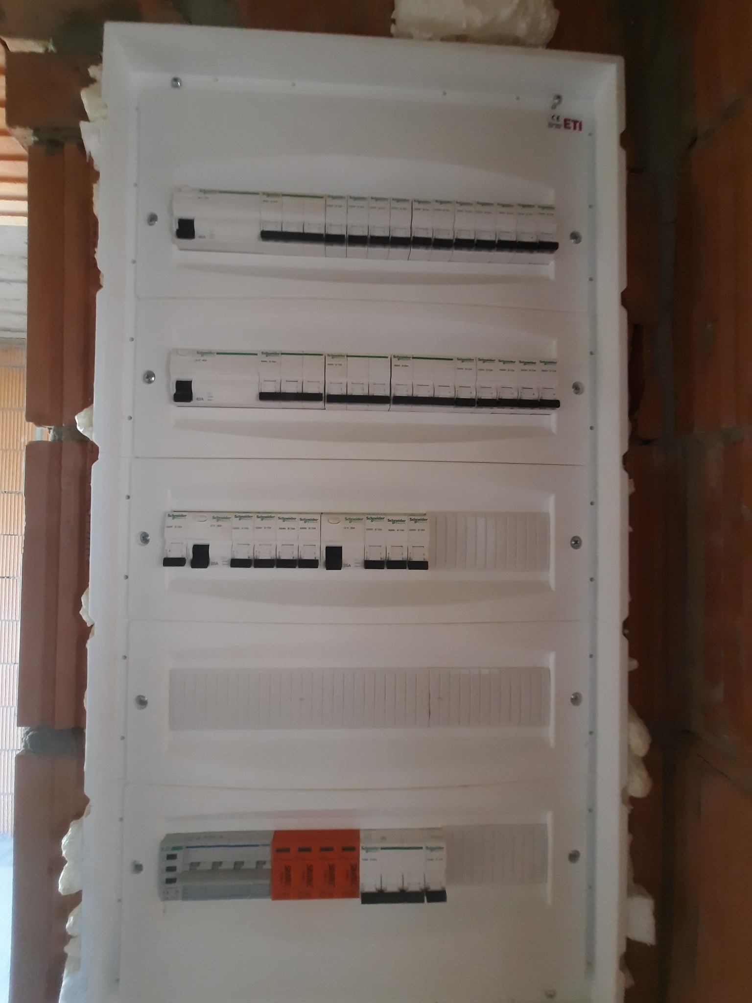 Rozdzielnica elektryczna z wyłącznikami różnicowoprądowymi i nadprądowymi zamontowana w ścianie z cegły, uszczelniona pianką montażową.