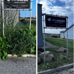 Tablica reklamowa firmy PanPaper z artykułami papierniczymi, prezentująca usługi wydruku, skanowania, laminowania, ksero i bindowania, umieszczona na metalowym stelażu przy chodniku, z widoczną...