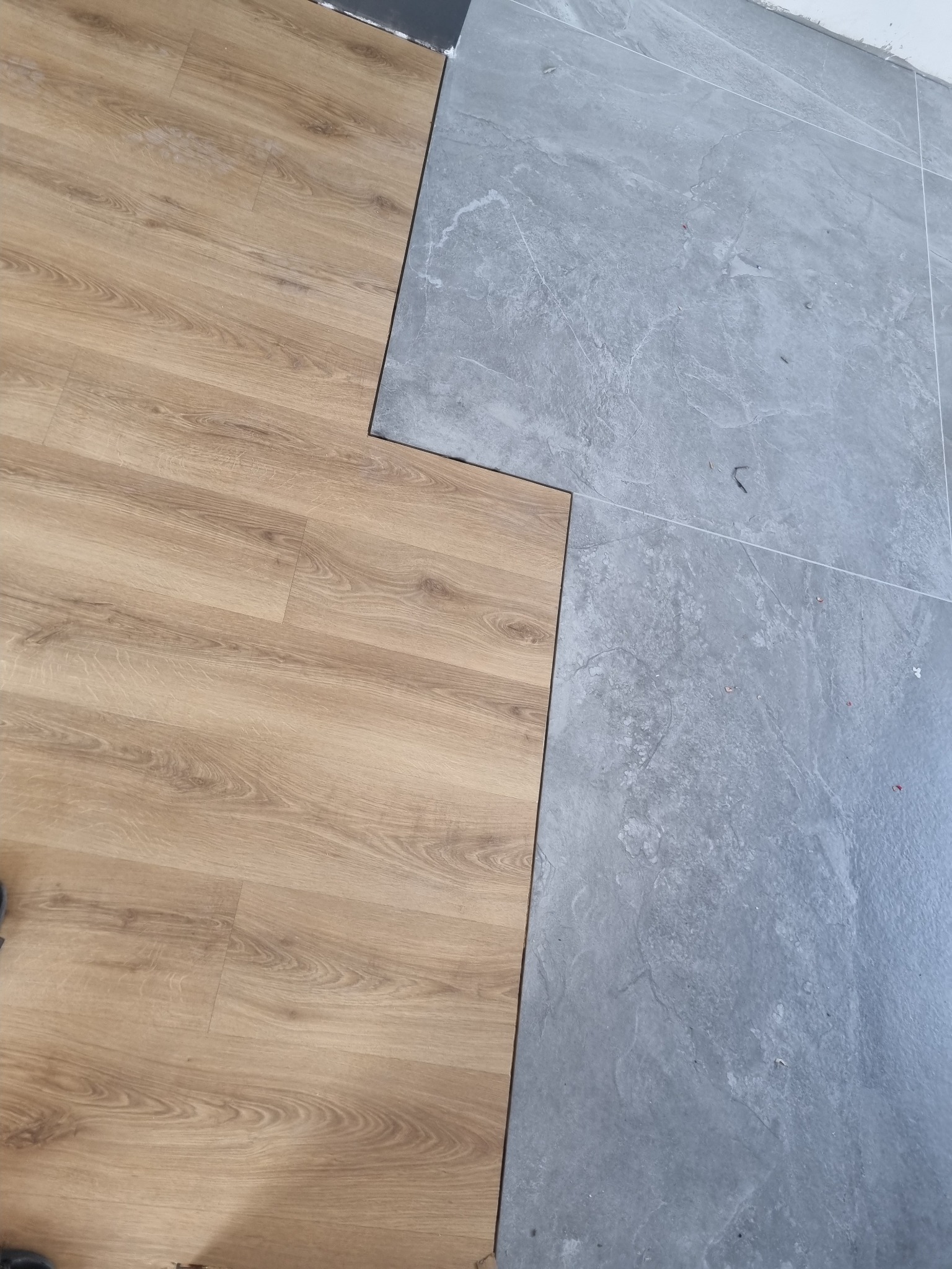 Fragment podłogi z widocznym połączeniem jasnych paneli imitujących drewno i szarych płytek ceramicznych o wzorze kamienia.