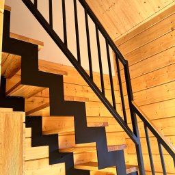 F.H.P Gawor Piotr Gawor - Nowoczesne schody z drewnianymi stopniami i czarną, metalową konstrukcją, w jasnym wnętrzu wykończonym drewnianą boazerią. Ujęcie z dołu, podkreślające geometrię.