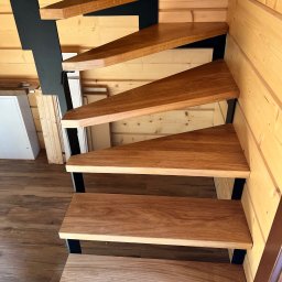 F.H.P Gawor Piotr Gawor - Nowoczesne schody z drewnianymi stopniami i czarną, metalową konstrukcją w domu z boazerią. Widok z dołu, ukazujący detale wykończenia i połączenie materiałów.