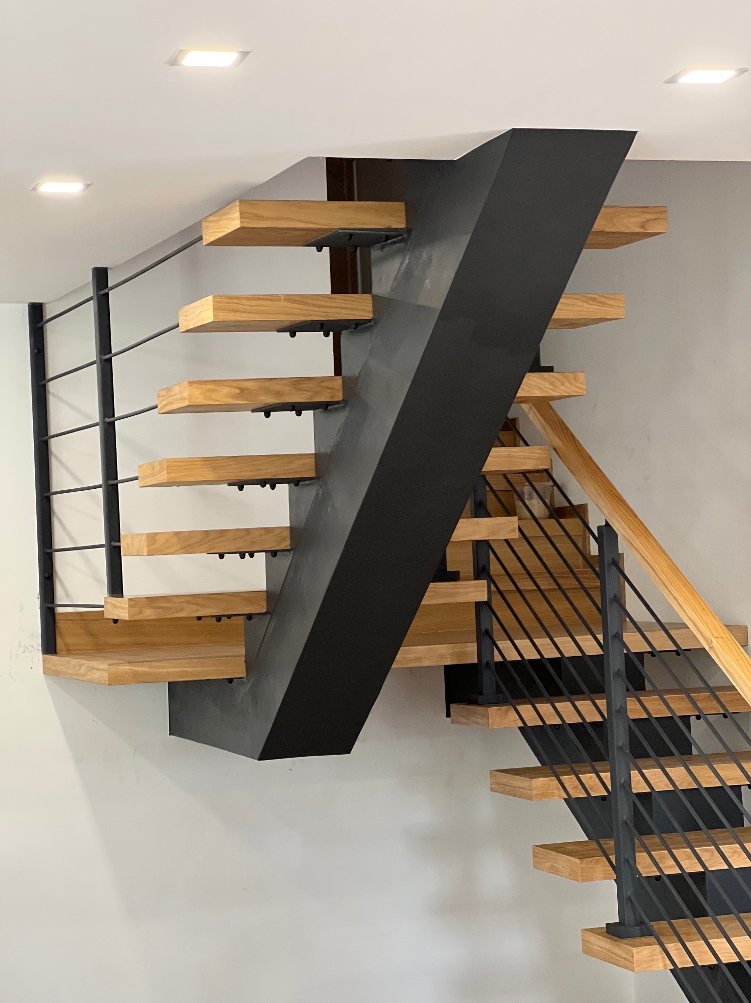 Nowoczesne schody z drewnianymi stopniami i metalową konstrukcją nośną w kolorze grafitowym. Minimalistyczne poręcze z cienkich prętów.