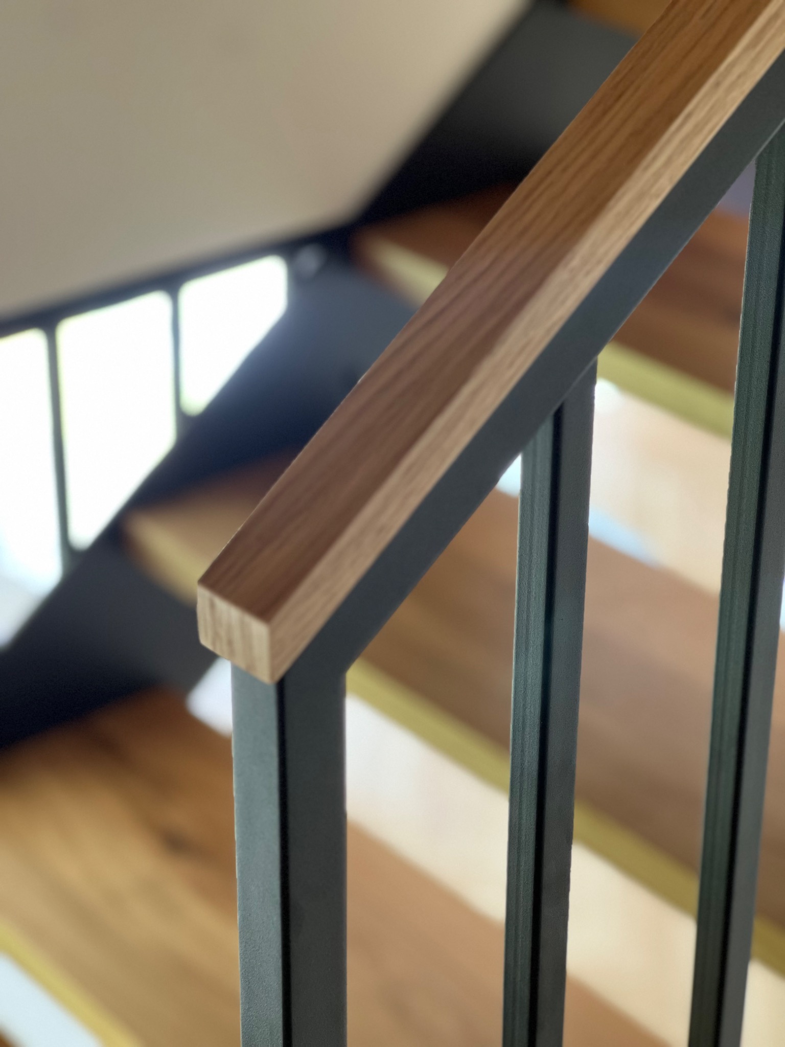 Nowoczesne schody z drewnianymi stopniami i metalową, grafitową balustradą z drewnianym poręczem. Ujęcie z dołu, widoczne fragmenty stopni.