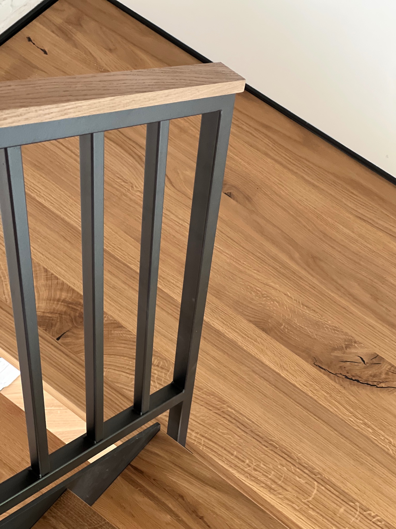 Nowoczesne schody z drewnianymi stopniami i minimalistyczną, metalową balustradą. Jasne drewno i szare metalowe elementy tworzą elegancki kontrast.