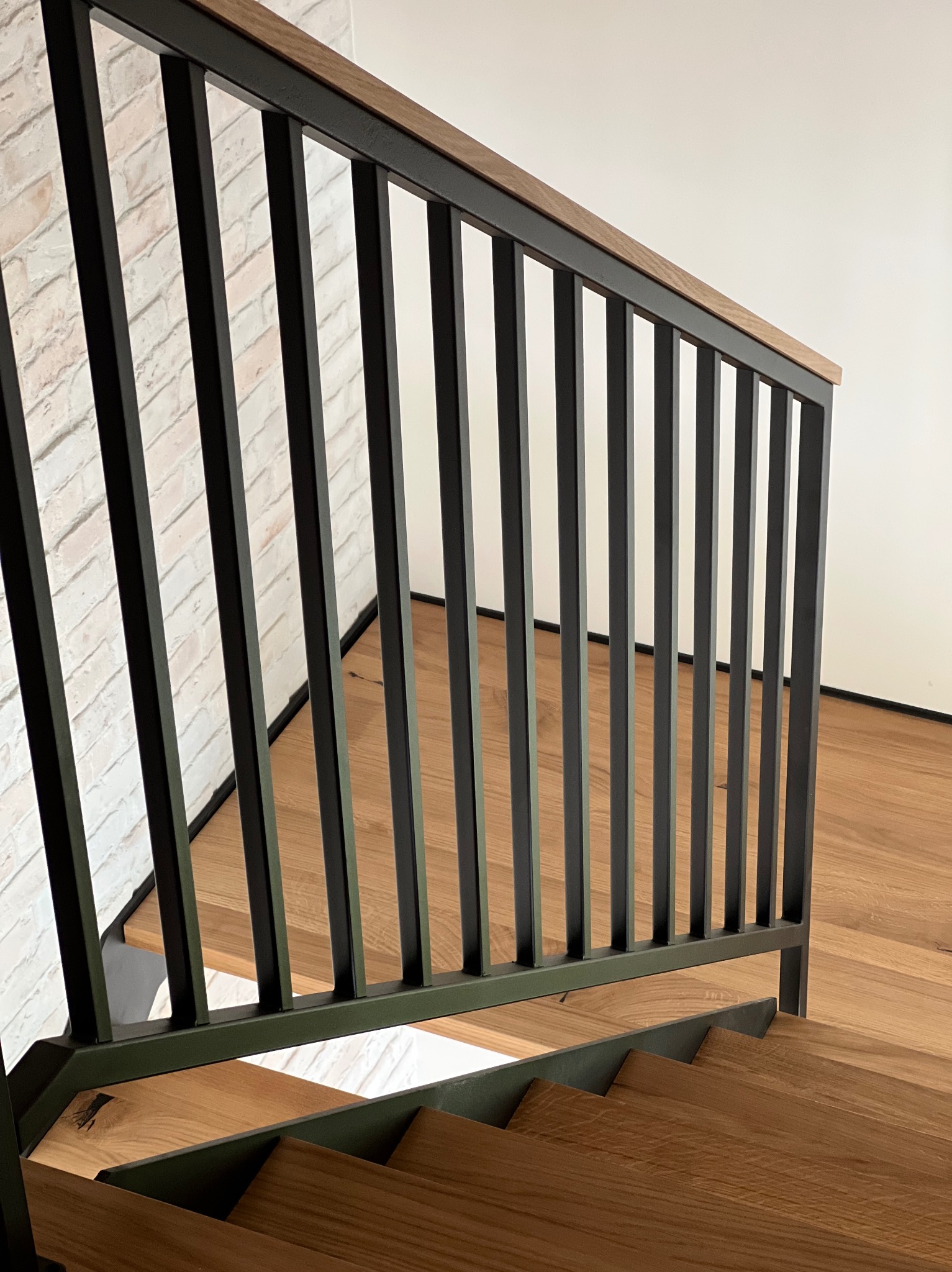 Nowoczesne schody z drewnianymi stopniami i czarną, metalową balustradą z drewnianym poręczem. Ściana z cegły w tle. Widok z dołu, ukazujący detale konstrukcji.