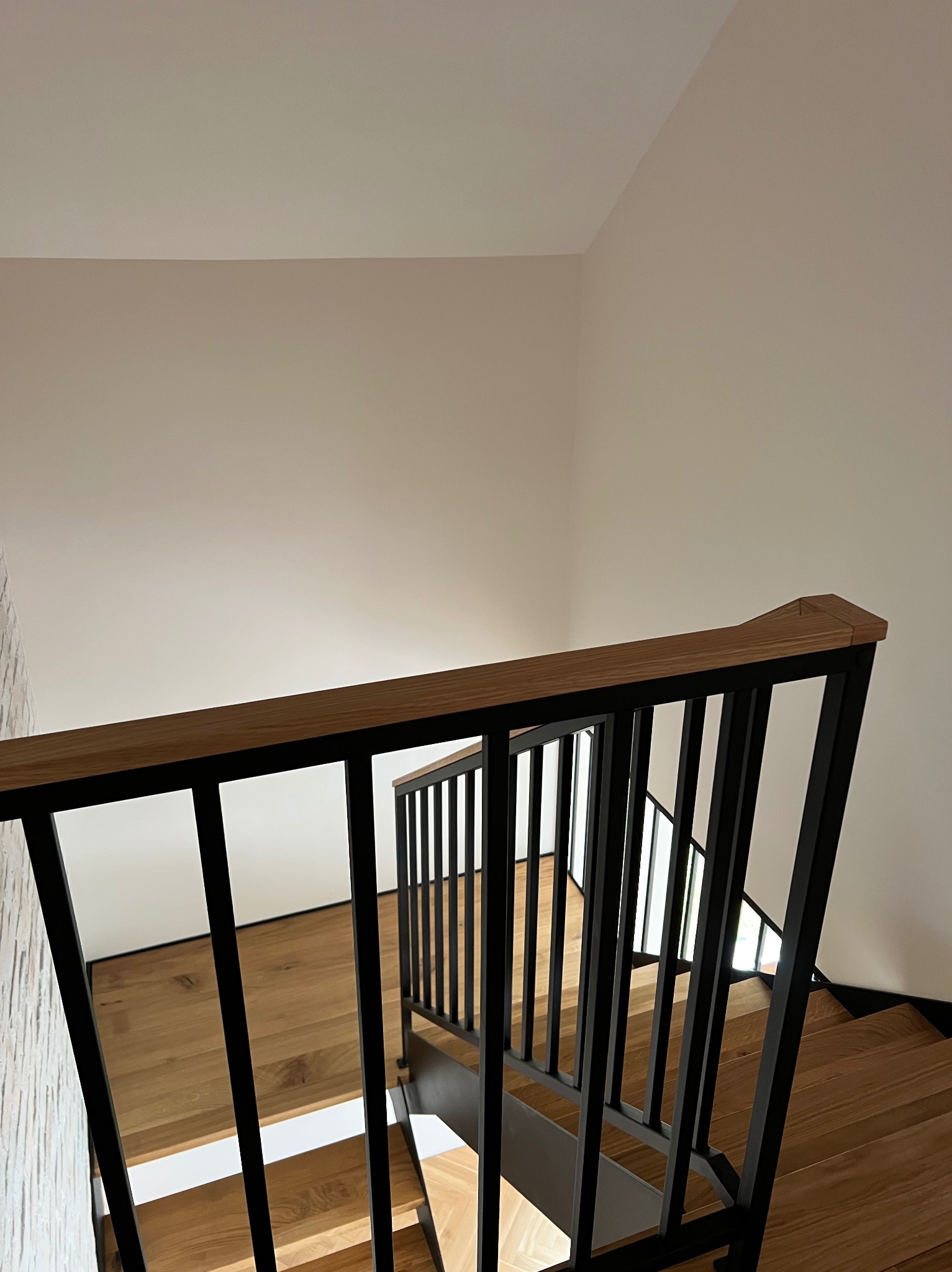 Nowoczesne schody drewniane z czarną metalową balustradą i drewnianą poręczą, widok z góry, jasne wnętrze, minimalistyczny design.
