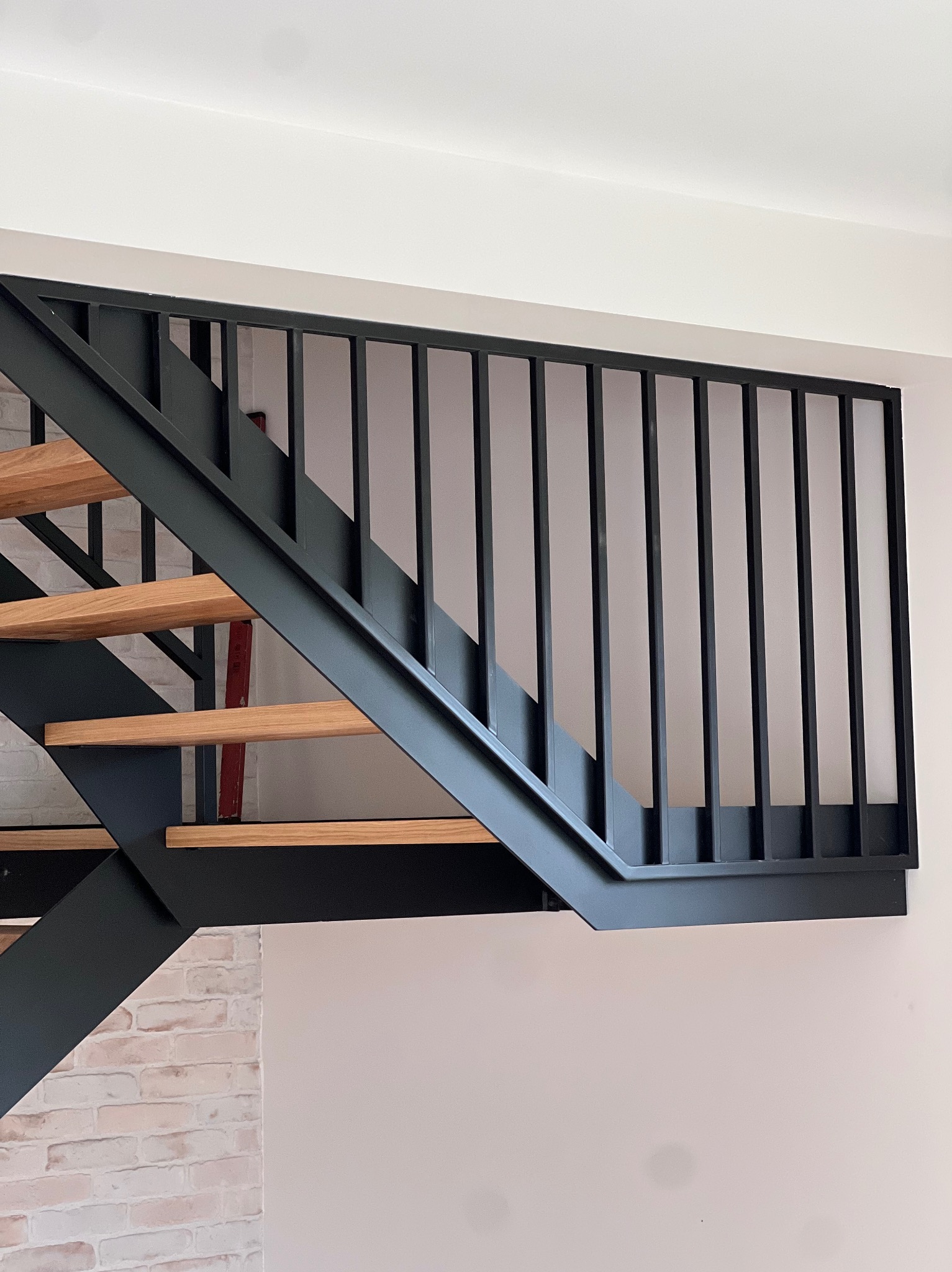 Nowoczesne schody z czarną metalową konstrukcją i drewnianymi stopniami, widoczne z dołu. Elementy ceglanej ściany w tle dodają unikalnego charakteru.