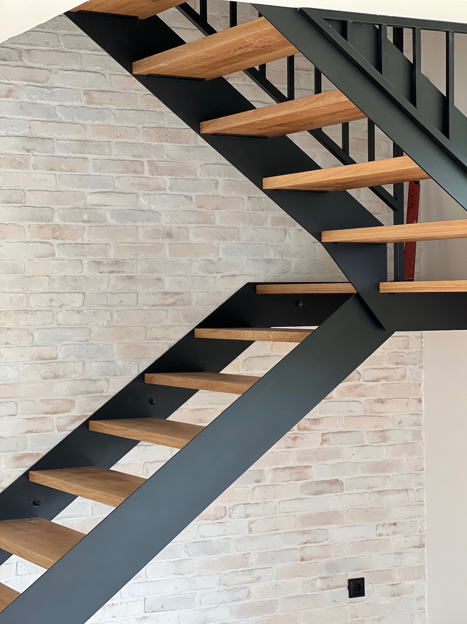 Nowoczesne schody z drewnianymi stopniami i metalową konstrukcją na tle ściany z białej cegły. Minimalistyczny design, widok z dołu.