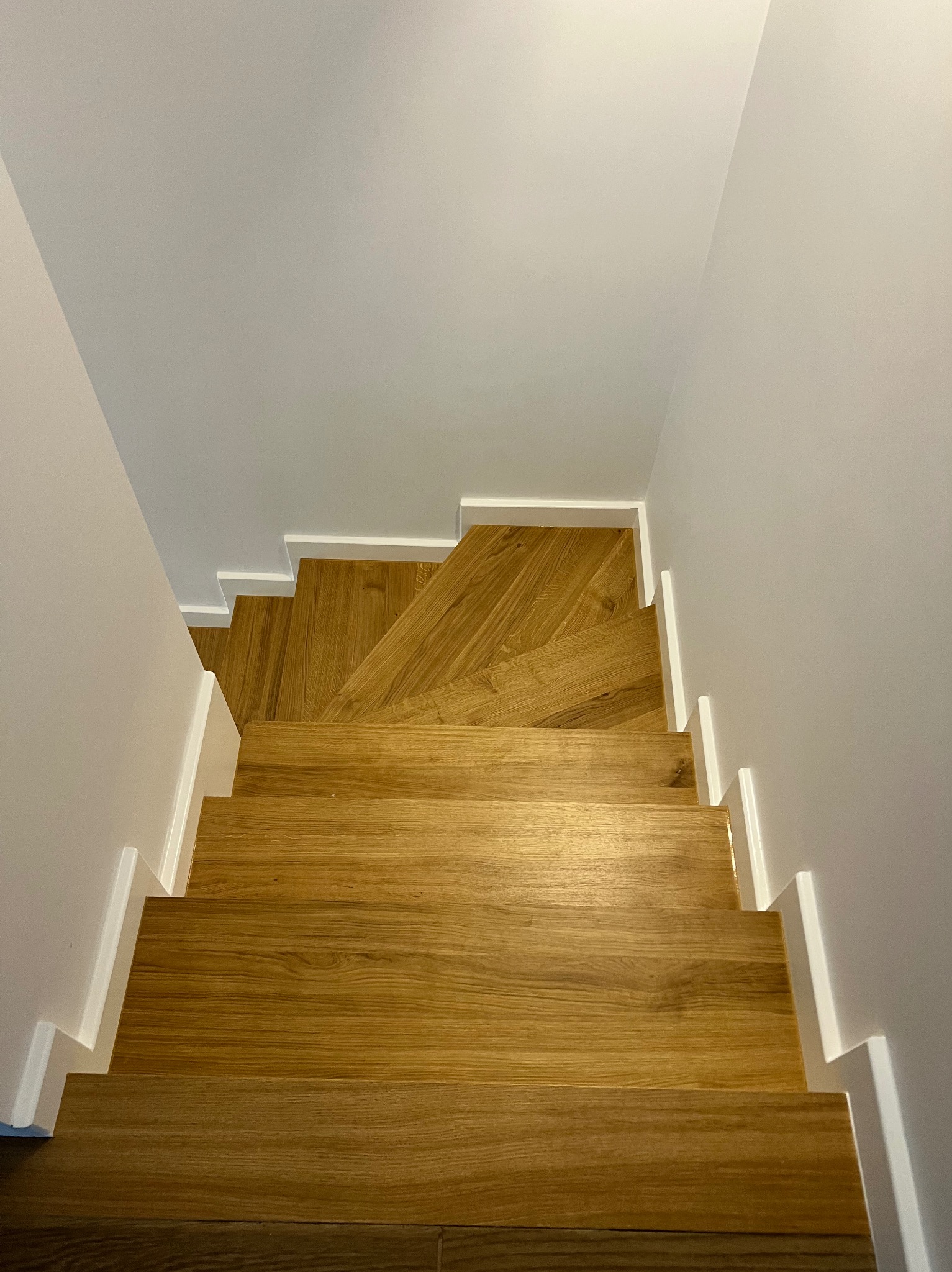 Nowoczesne schody drewniane z białymi listwami przypodłogowymi, widok z góry. Jasne drewno, minimalistyczny design, czyste linie, subtelne oświetlenie.