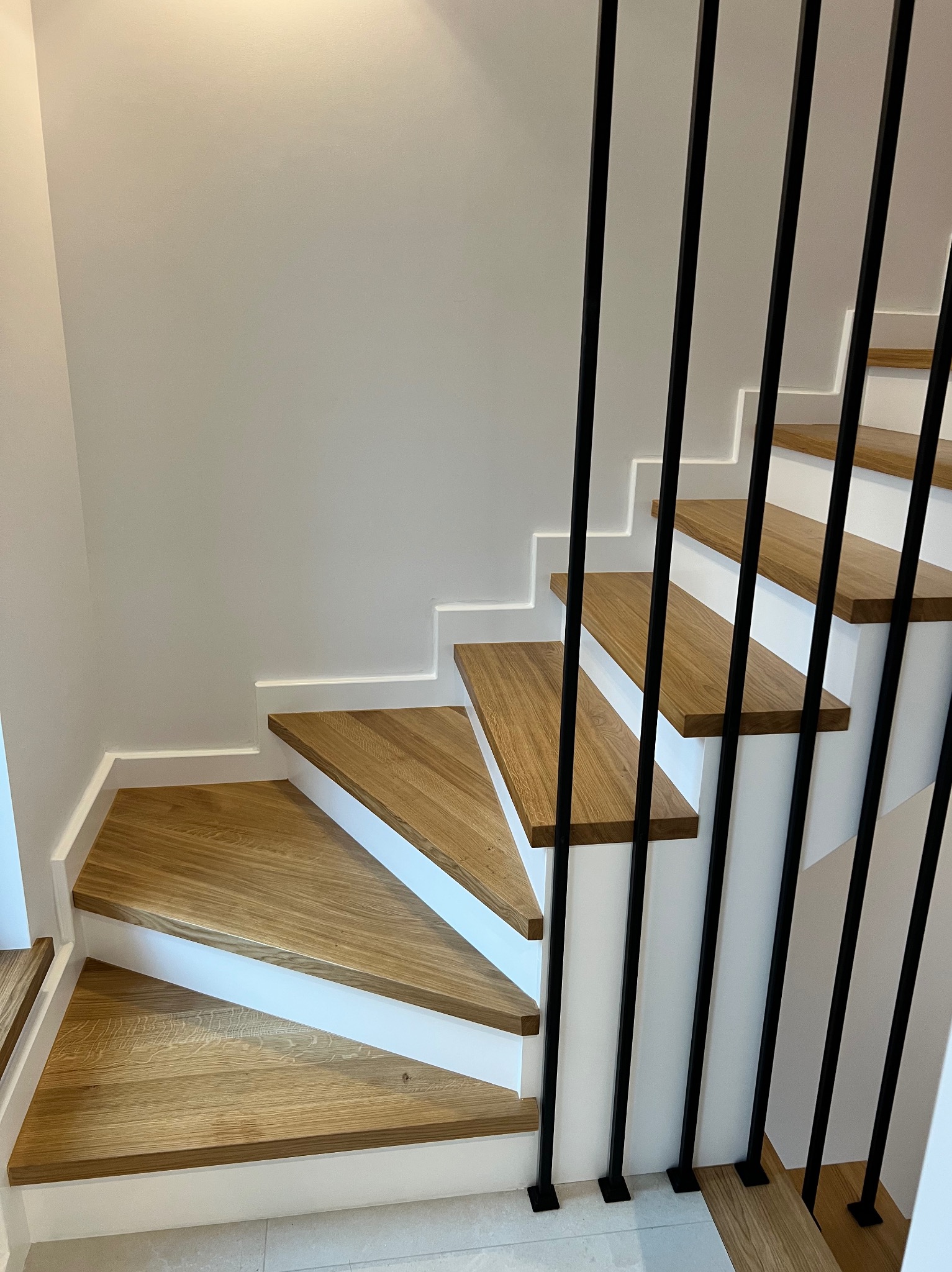 Nowoczesne schody z drewnianymi stopniami i czarną, minimalistyczną balustradą. Białe wykończenie krawędzi stopni. Ujęcie z dołu, podkreślające geometrię.