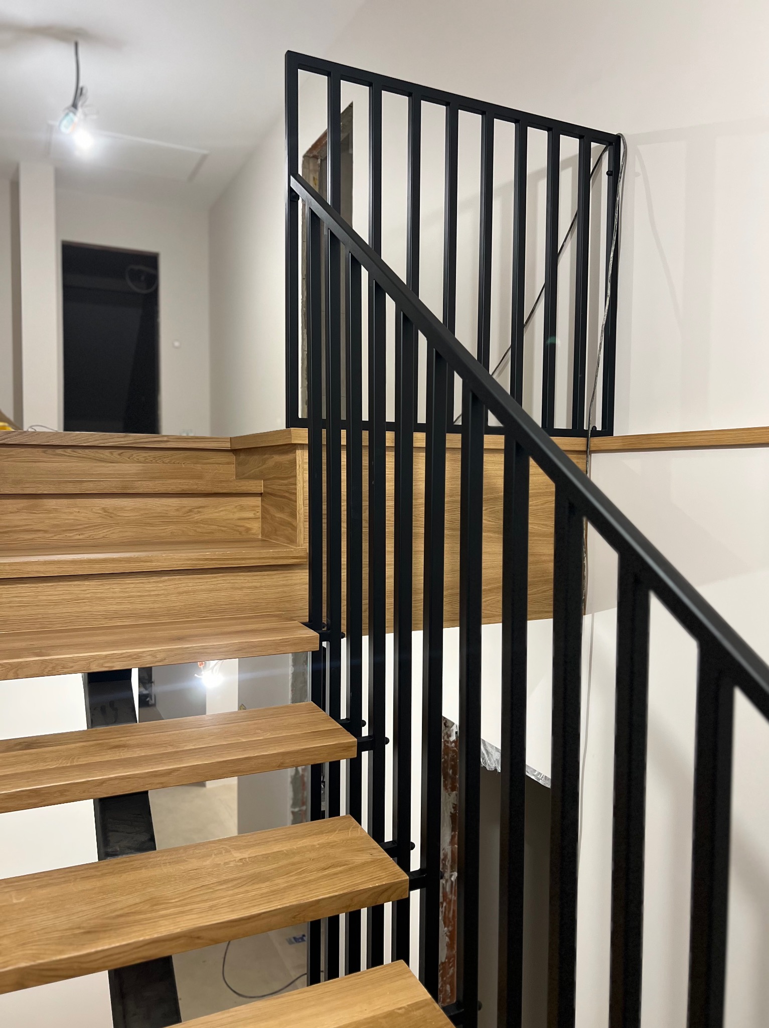 Drewniane schody z czarną, metalową balustradą w nowoczesnym wnętrzu. Widoczne stopnie z naturalnego drewna i minimalistyczny design poręczy.