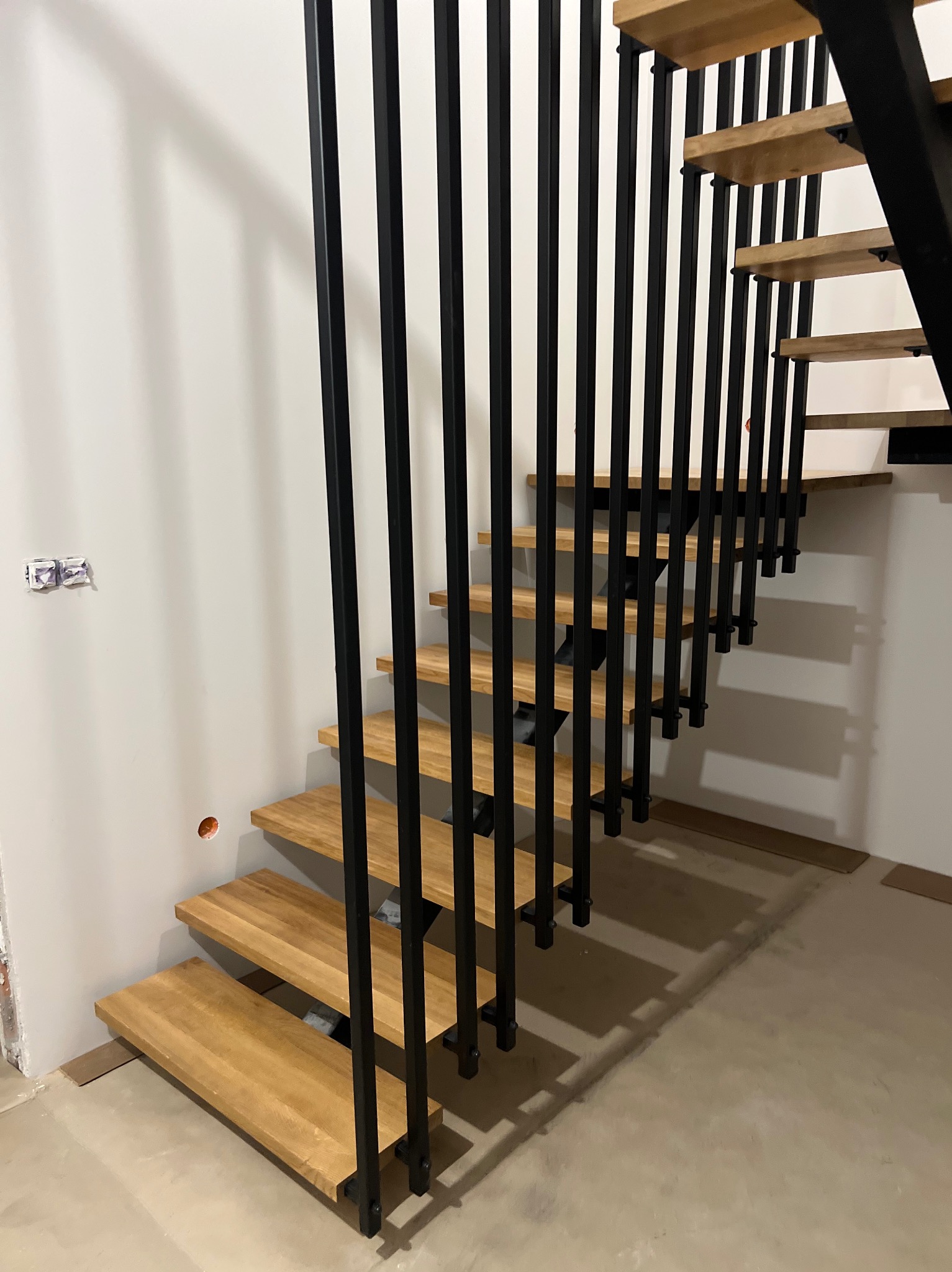 Nowoczesne schody z drewnianymi stopniami i czarnymi, metalowymi balustradami. Minimalistyczny design, jasne drewno, surowe wykończenie ścian.